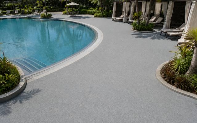 Pale rubber surfacing around a resort-style pool with cabanas behind it.